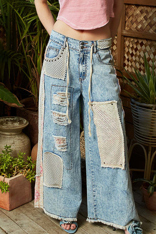 Person wearing patchwork jeans with a pink top in an outdoor setting with plants.