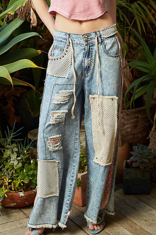 Person wearing patchwork jeans standing among potted plants