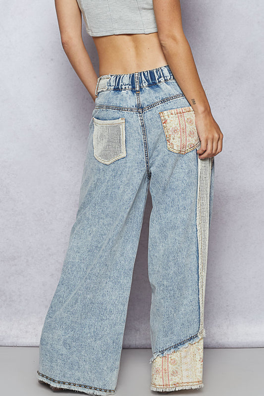 Person wearing light blue jeans with decorative patches on a plain background