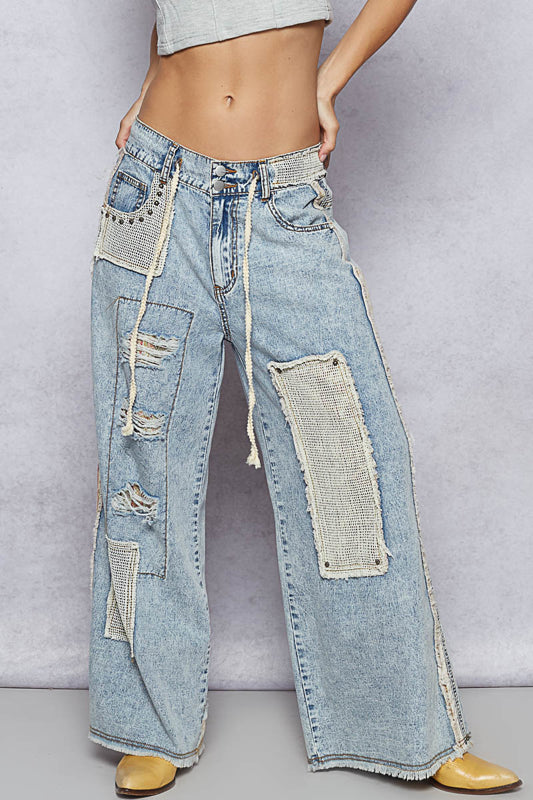 Light blue jeans with patchwork design worn by a person on a gray background