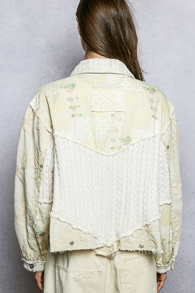 Person wearing a light-colored, textured jacket with floral patterns on a plain background