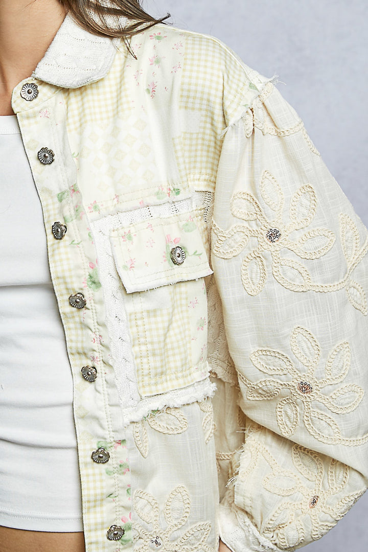 Close-up of a cream-colored embroidered jacket with floral patterns on a plain background