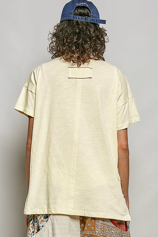 Person wearing a beige t-shirt and patterned pants with a blue cap on a plain background