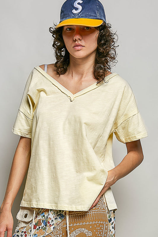 Person wearing a light yellow top and patterned pants with a cap on a plain background