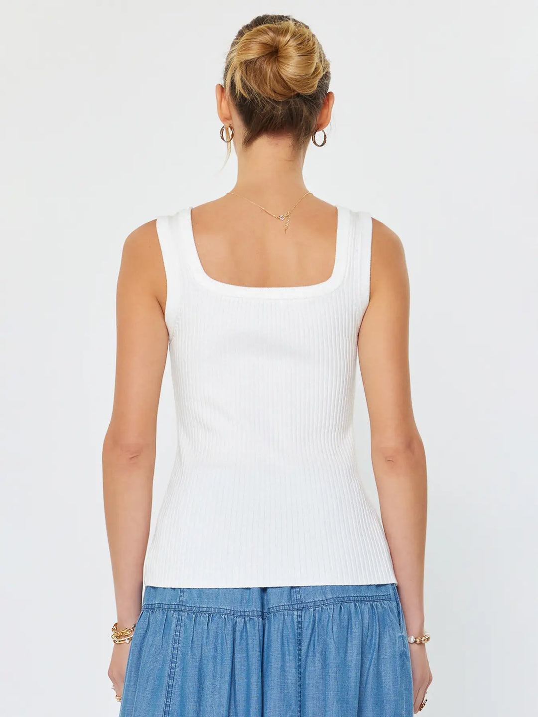 Woman wearing a white tank top and blue skirt on a plain background