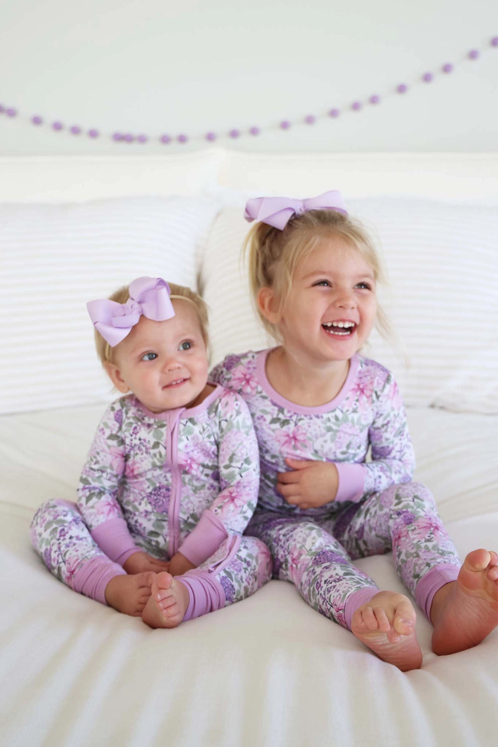 Two young children in matching floral pajamas sitting on a white surface.