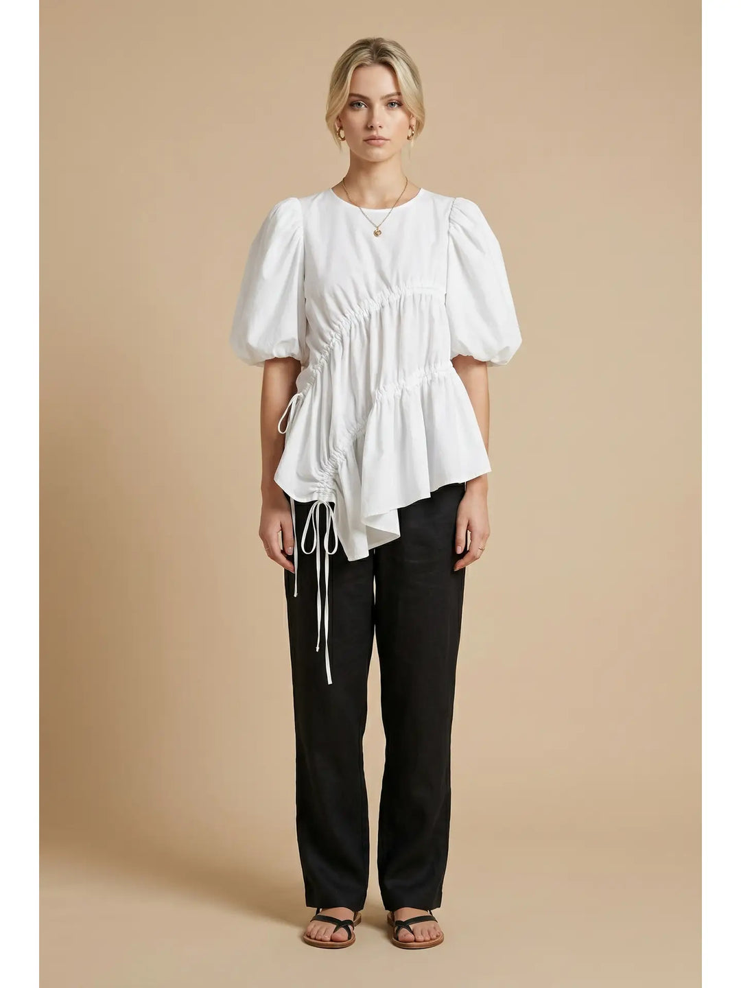 Woman wearing a white blouse with puffed sleeves and black pants on a beige background