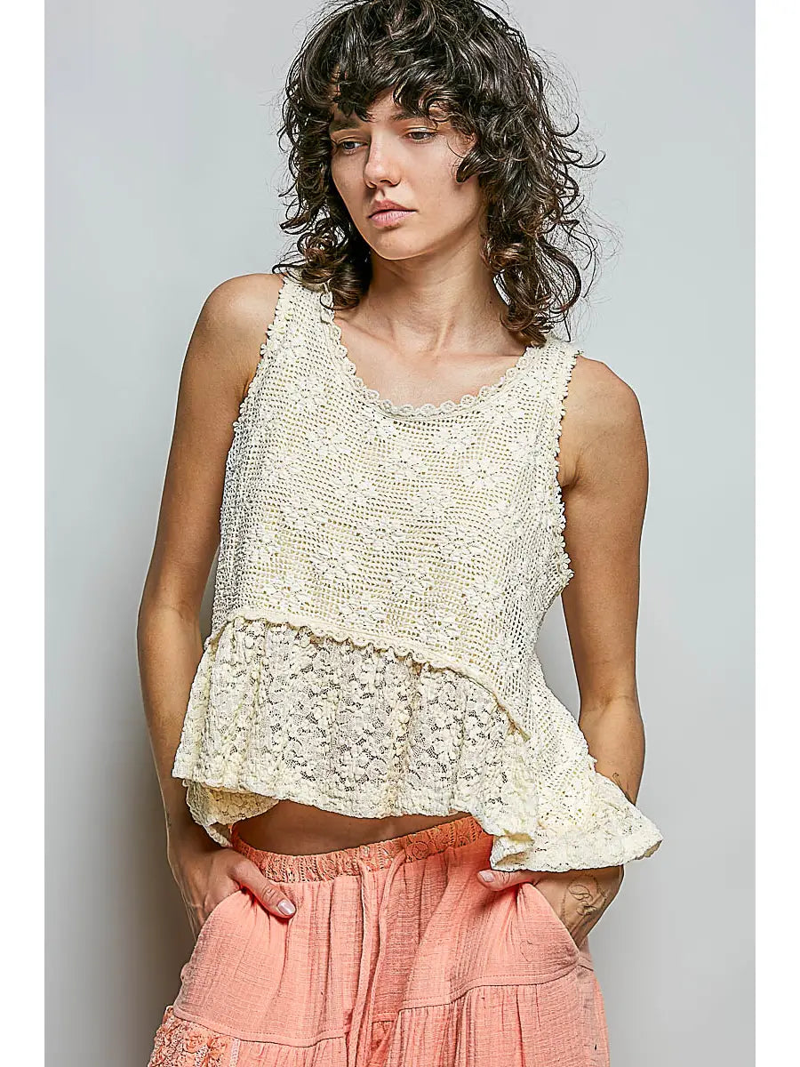 Woman wearing a beige lace top and pink pants against a plain background