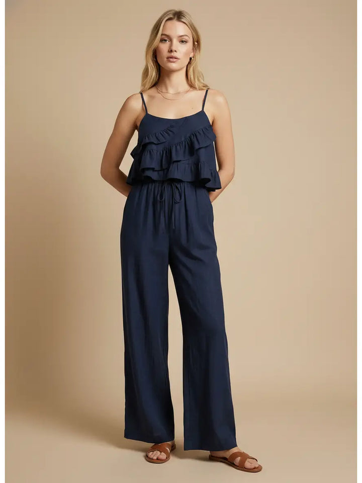 Woman wearing a navy blue jumpsuit with ruffled top on a beige background