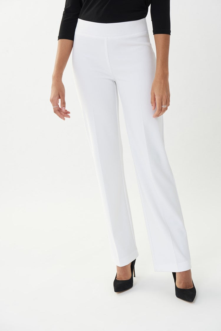 A model wearing white pleated pants and black shoes, against a plain background.