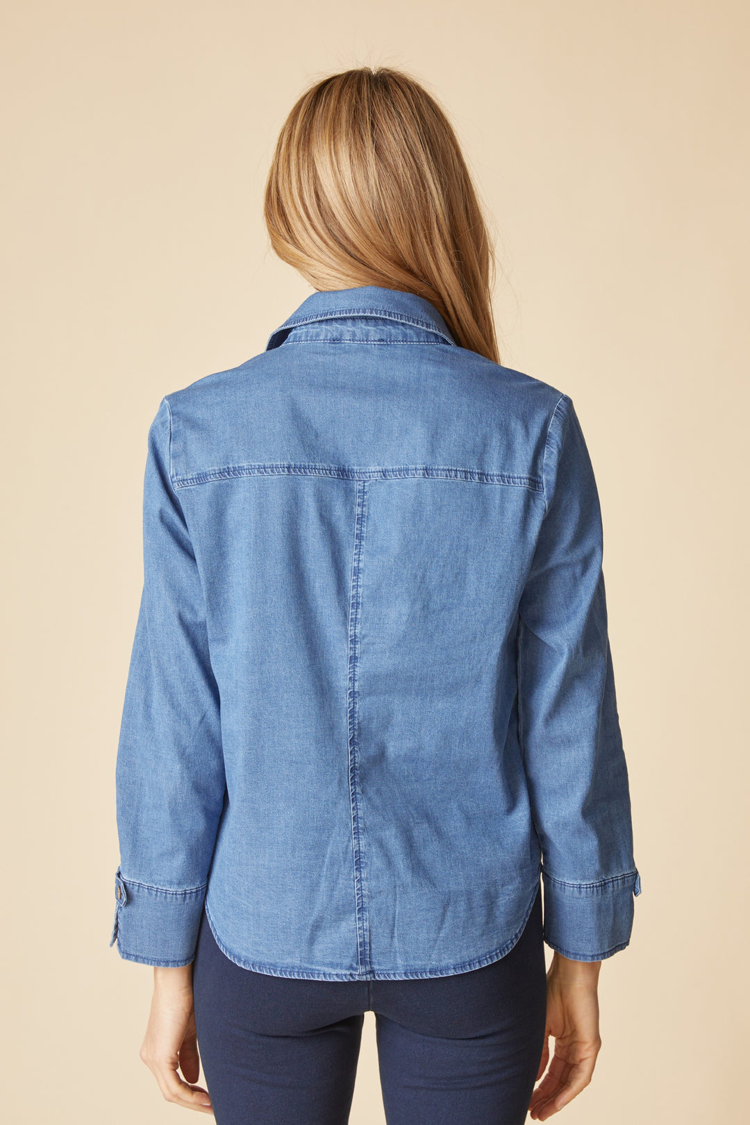 Person wearing a blue denim jacket on a beige background