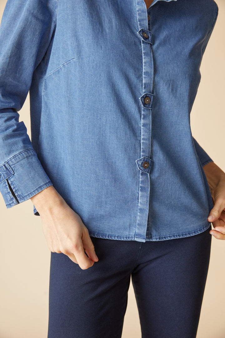 Person wearing a blue denim shirt and dark pants on a beige background