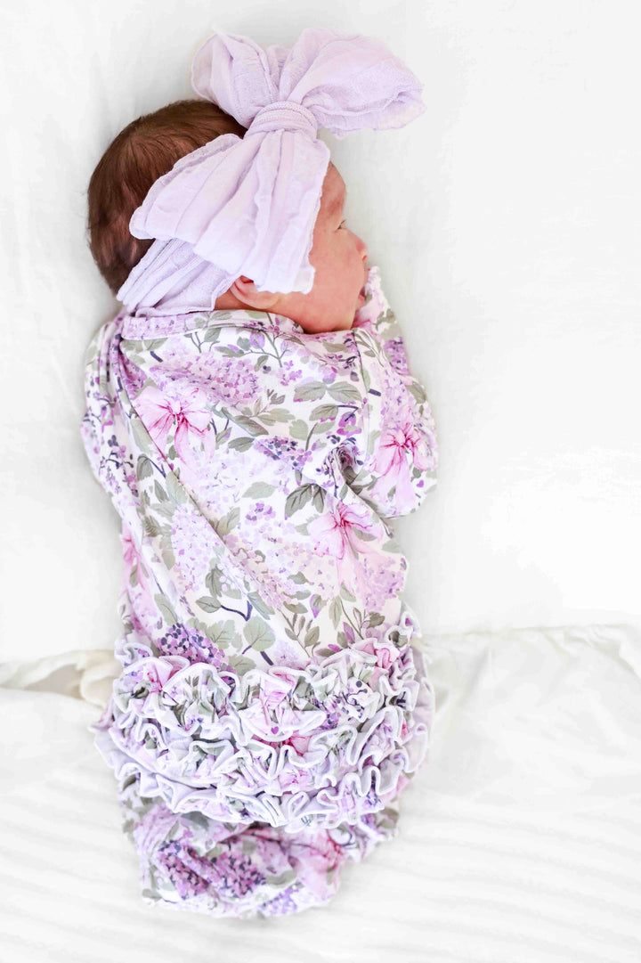 Baby wrapped in a floral swaddle with a matching headband on a white background