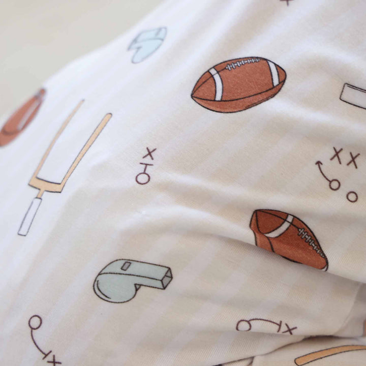 Close-up of fabric with sports-themed pattern including footballs, a baseball bat, and a whistle on a beige background.