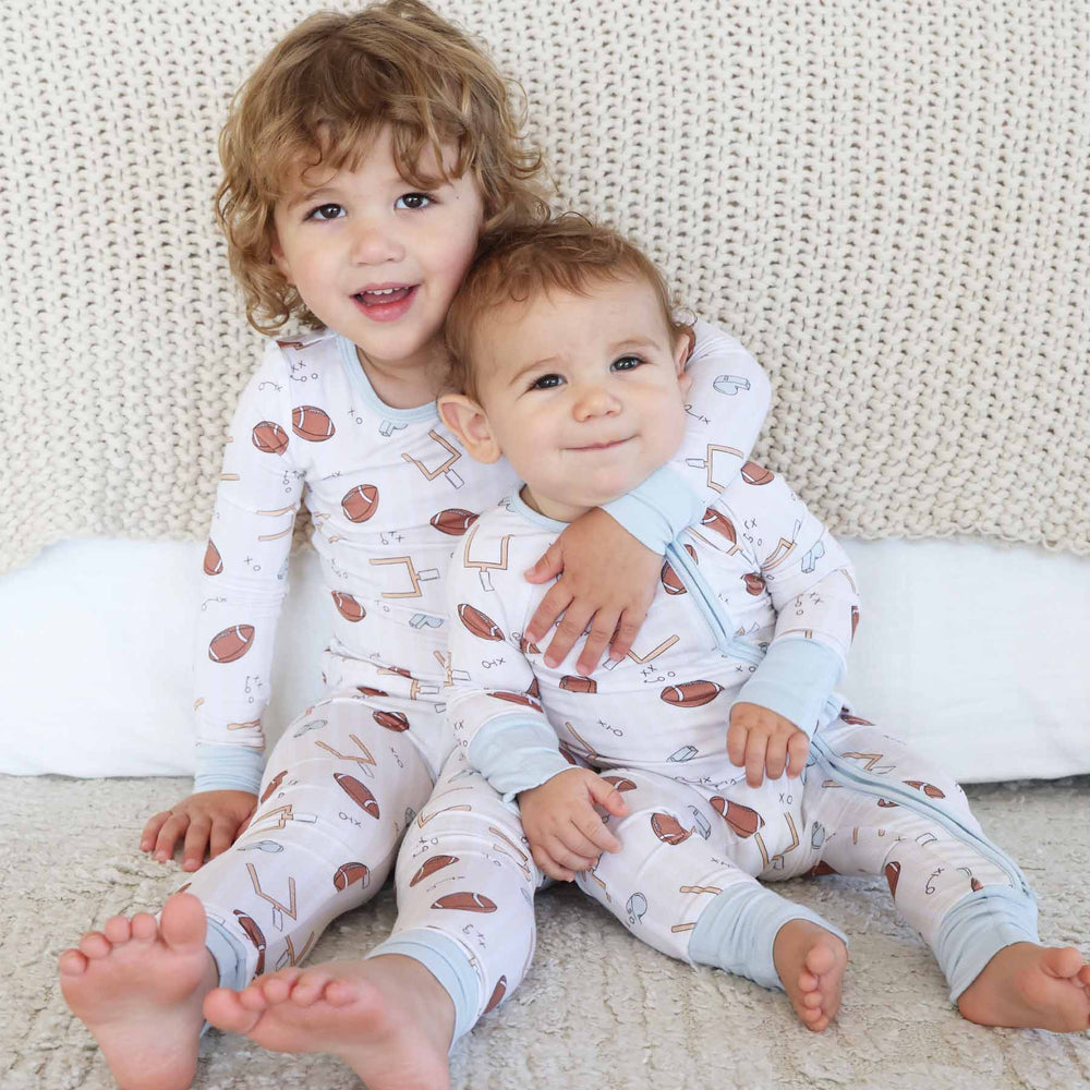 Two children wearing matching pajamas with a pattern of hearts and arrows, sitting on a textured surface.