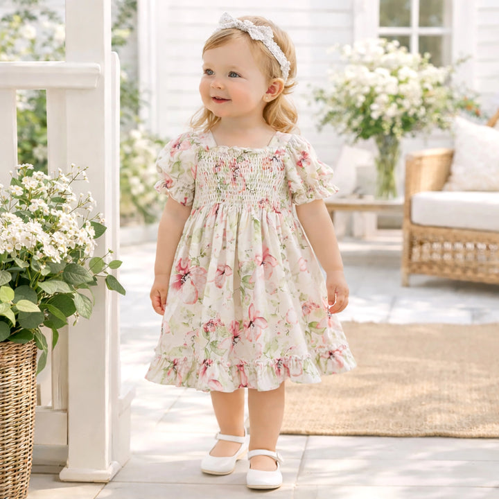 Young girl in a floral dress standing on a porch with flowers and furniture in the background