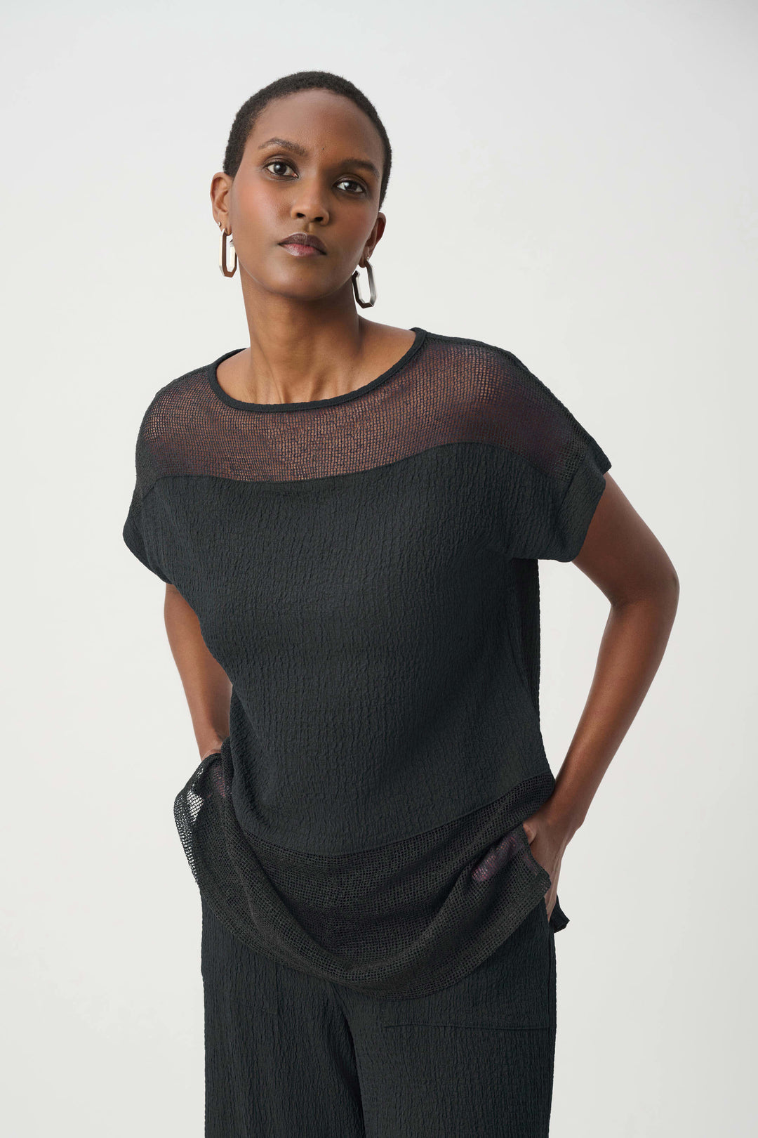 Woman wearing a black outfit with sheer sleeves against a white background