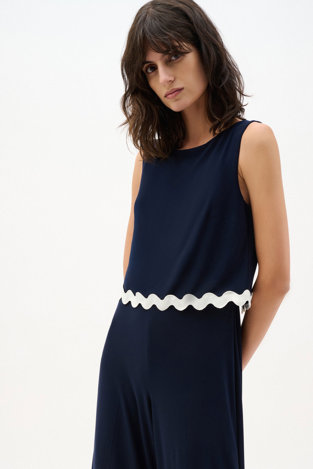 Woman wearing a navy dress with a white scalloped hem on a white background