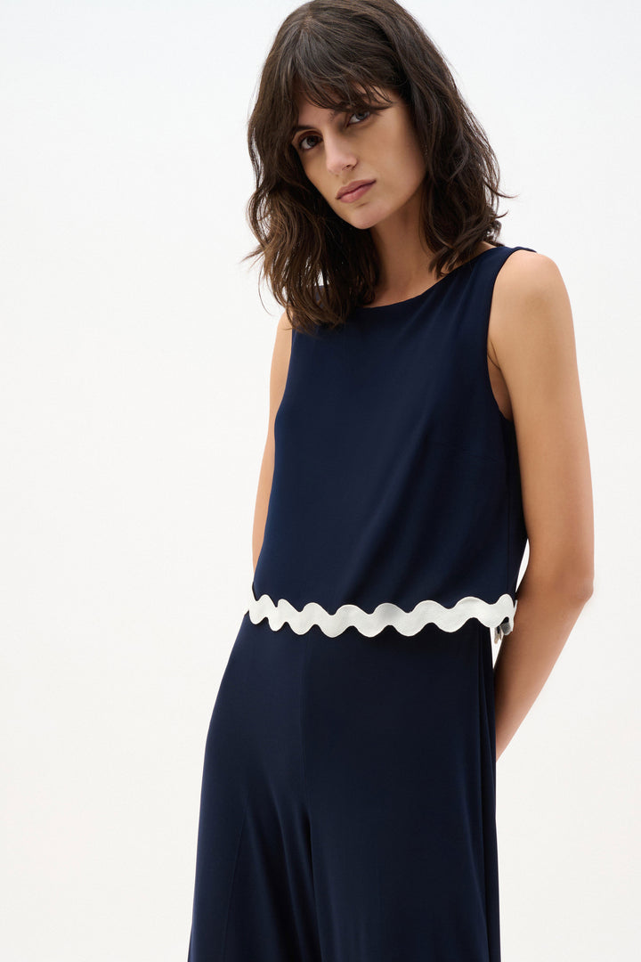Woman wearing a navy dress with a white scalloped hem on a white background