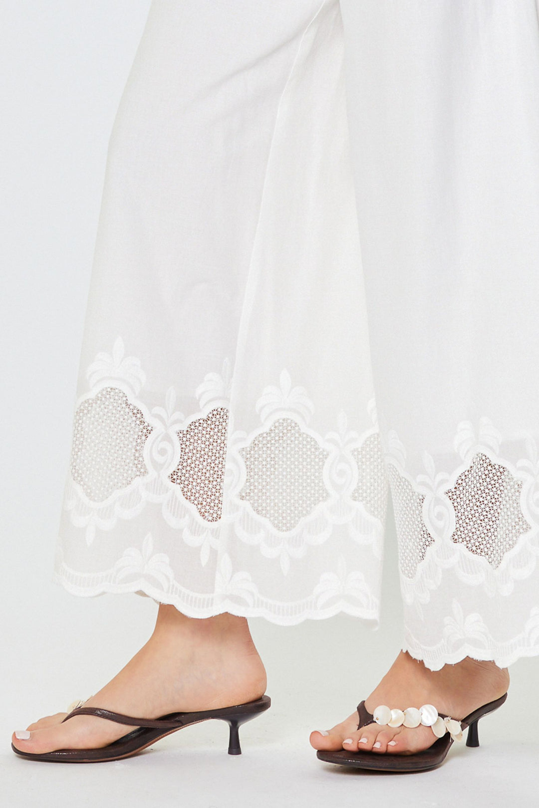 White lace-trimmed pants with black high-heeled sandals on a white background