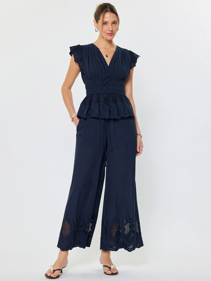 Woman wearing a navy blue peplum top and wide-leg pants on a white background