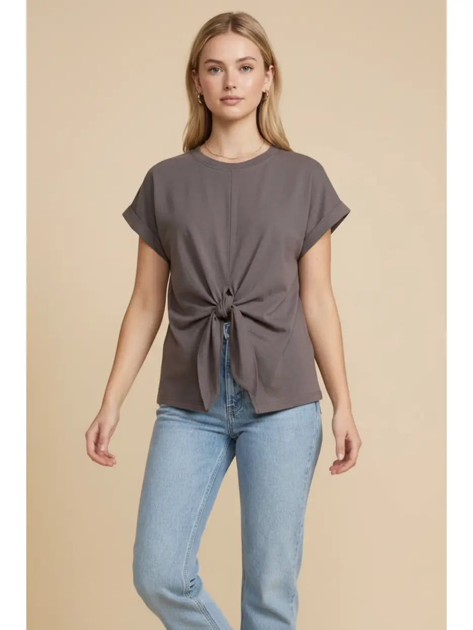 Woman wearing a brown knot-front top and blue jeans on a beige background