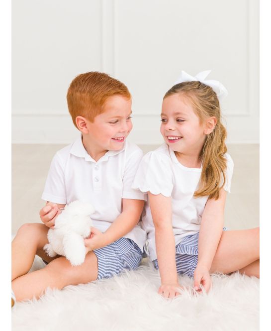 Two children sitting on a white surface, smiling and holding a fluffy toy.
