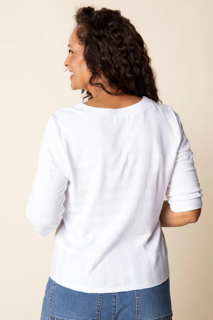 Woman wearing a white long-sleeve top and blue jeans on a beige background