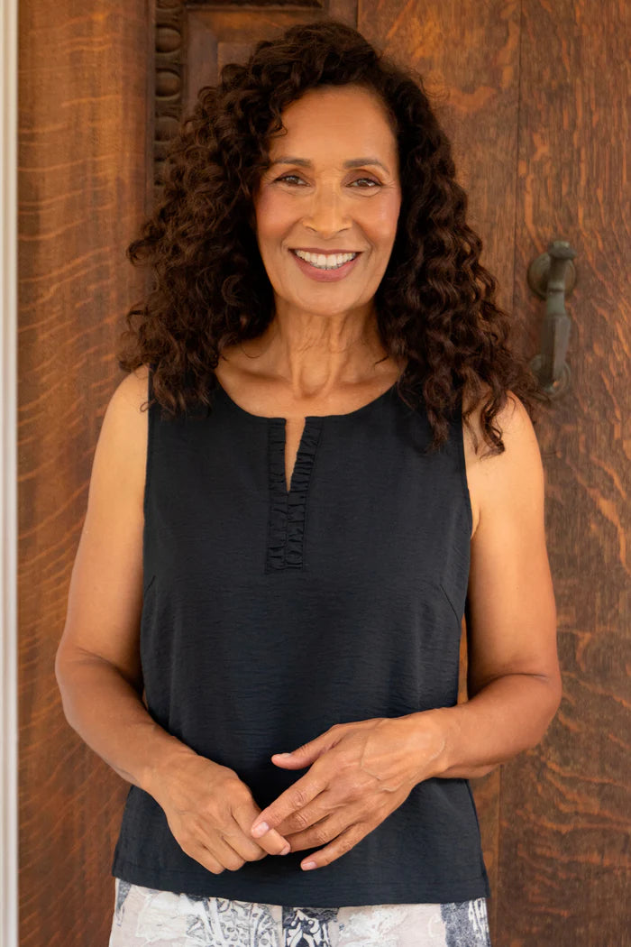 Woman wearing a black sleeveless top standing in front of a wooden door.