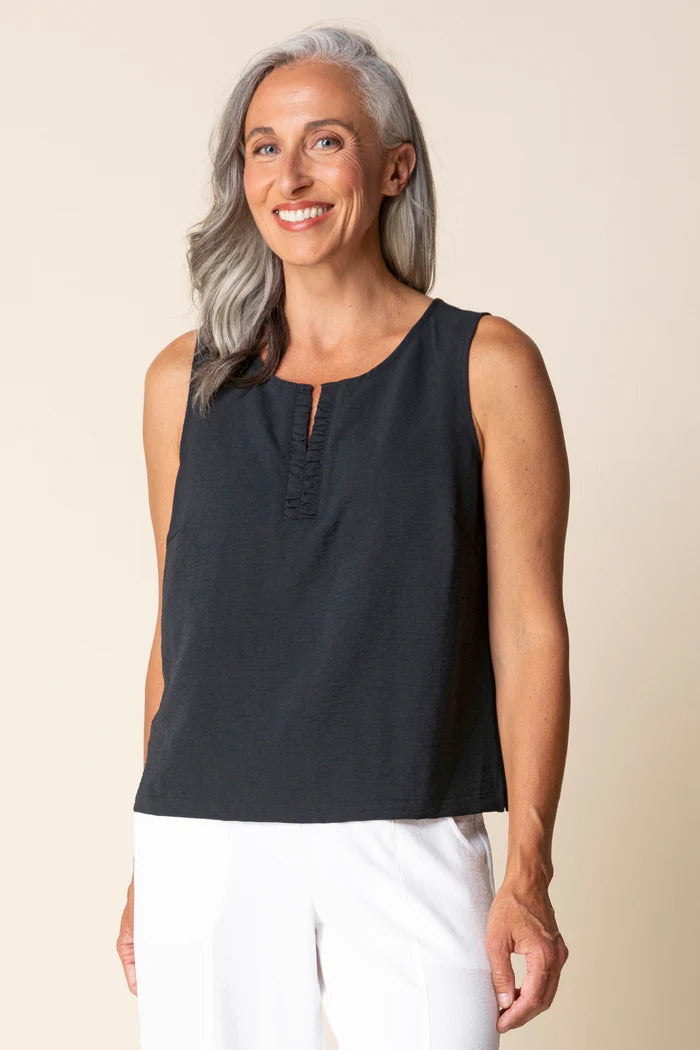 Woman wearing a black sleeveless top and white pants against a beige background
