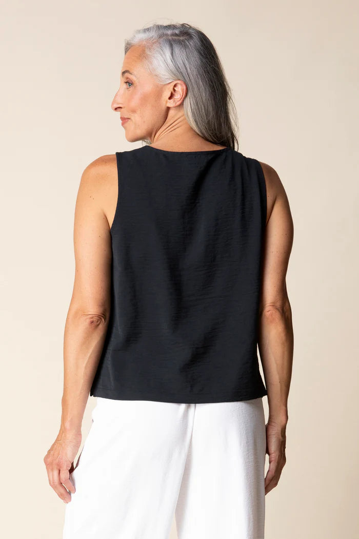 Woman wearing a black sleeveless top and white pants against a beige background