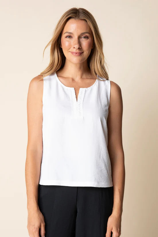 Woman wearing a white sleeveless top and black pants against a beige background