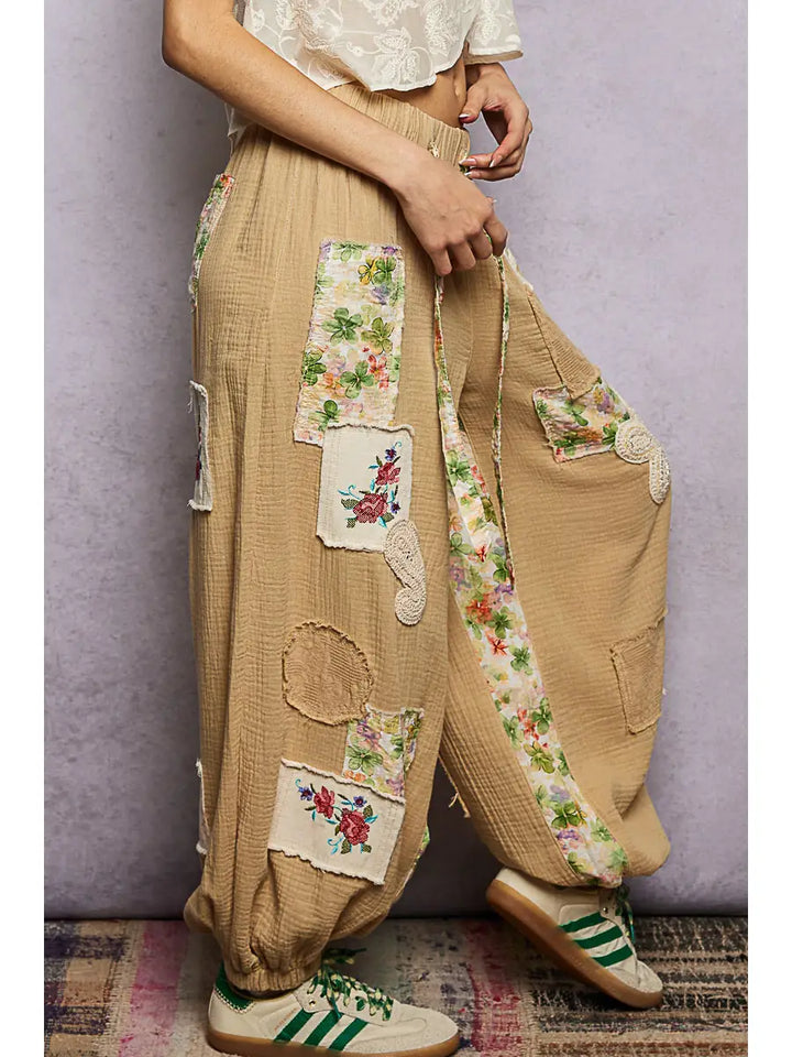 Beige pants with floral patches worn by a person against a plain background