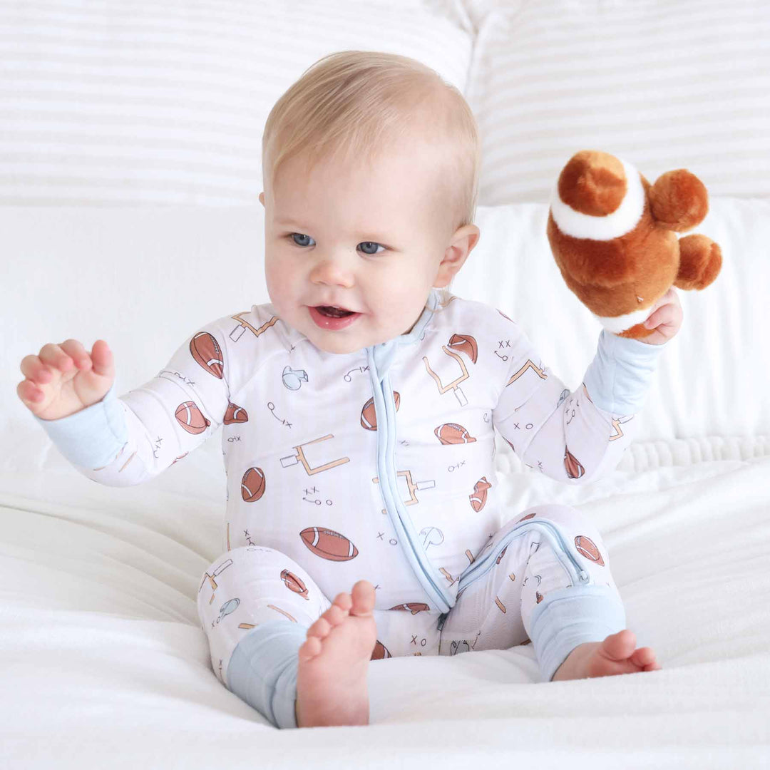 Baby in a patterned onesie holding a toy on a white blanket
