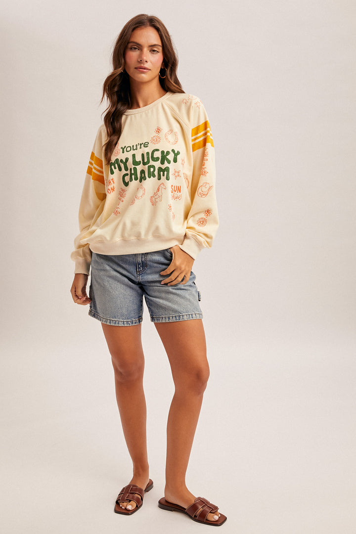 Woman wearing a cream-colored sweatshirt with text and graphics, paired with denim shorts on a light gray background.