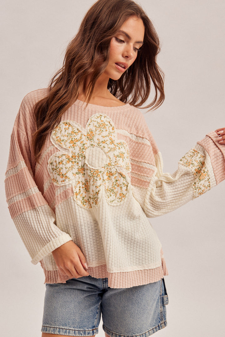 Woman wearing a pink and white embroidered sweater with denim shorts on a plain background