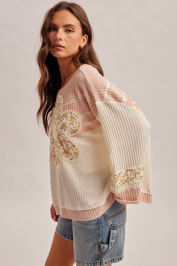 Woman wearing a light pink embroidered top with denim shorts on a plain background