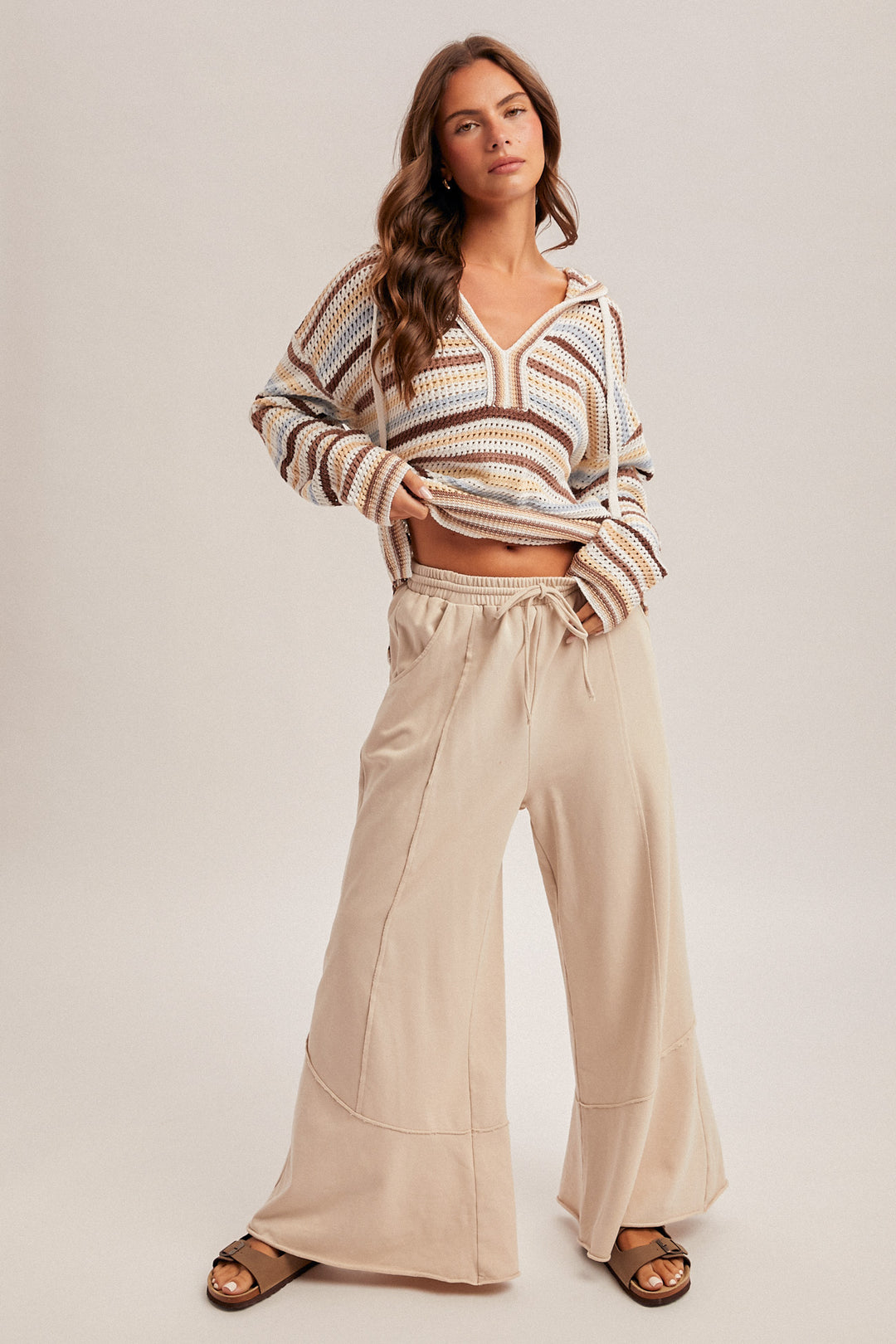 Woman wearing a striped sweater and beige wide-leg pants on a plain background