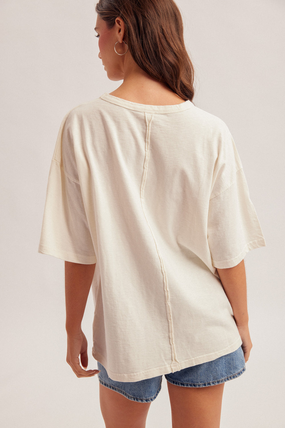 Woman wearing a beige oversized t-shirt and denim shorts on a plain background