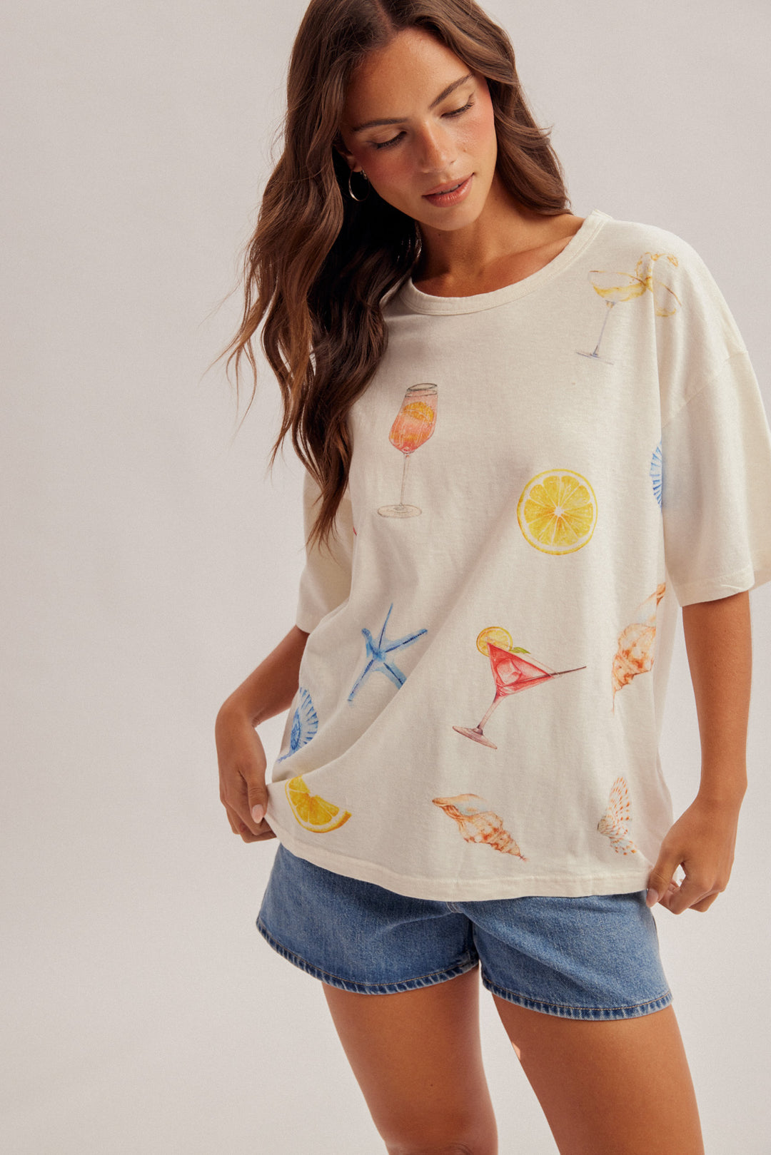 Woman wearing a cream-colored t-shirt with colorful graphics on a plain background
