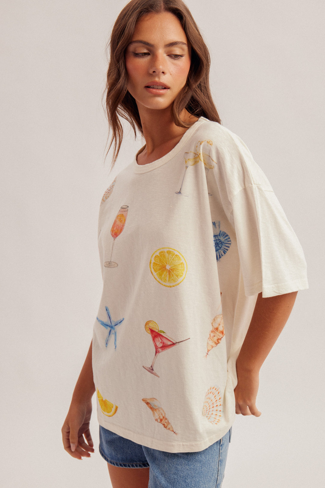 Woman wearing a white oversized t-shirt with colorful graphics on a plain background