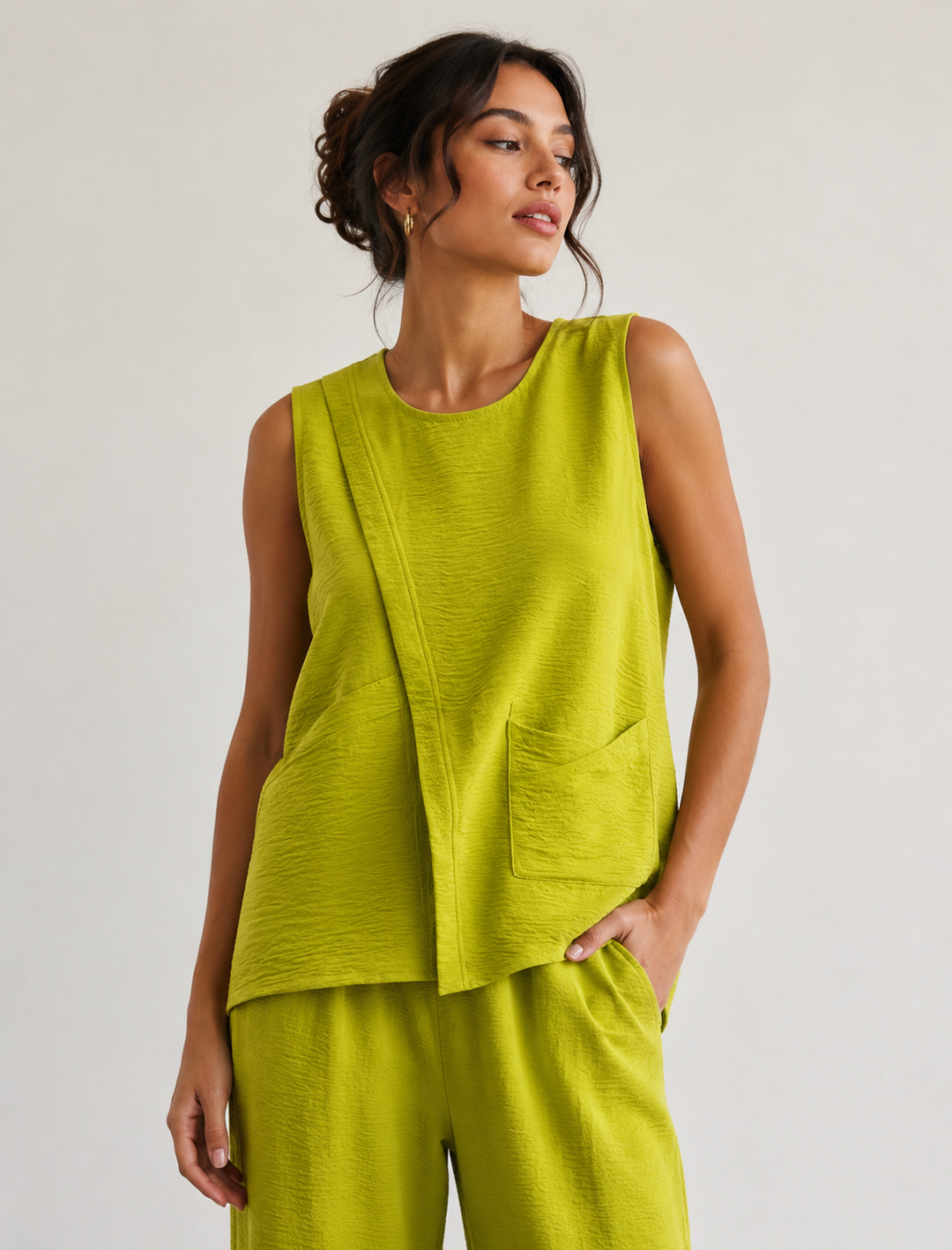 Woman wearing a green sleeveless top and pants against a plain background