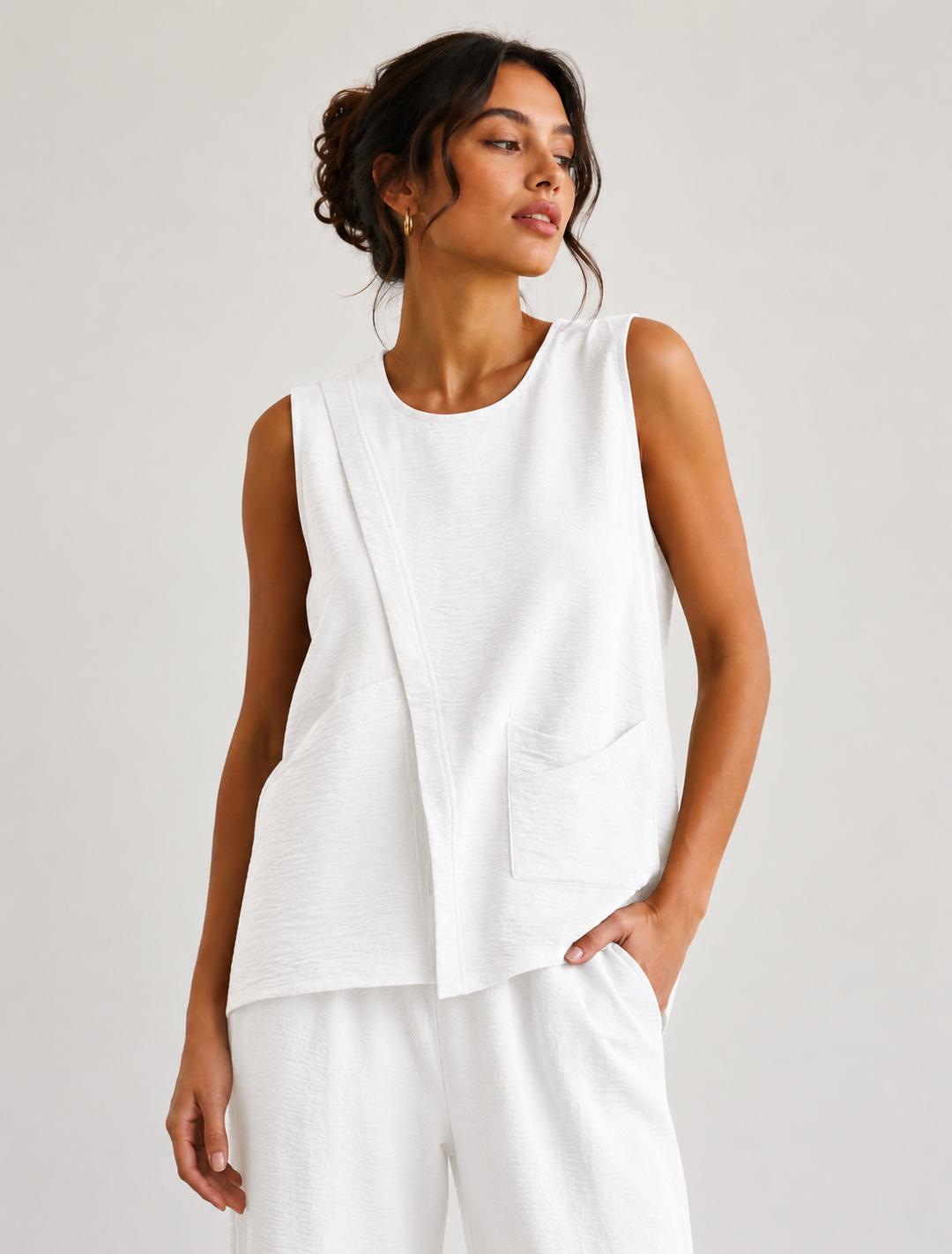 Woman wearing a white sleeveless top and pants against a plain background