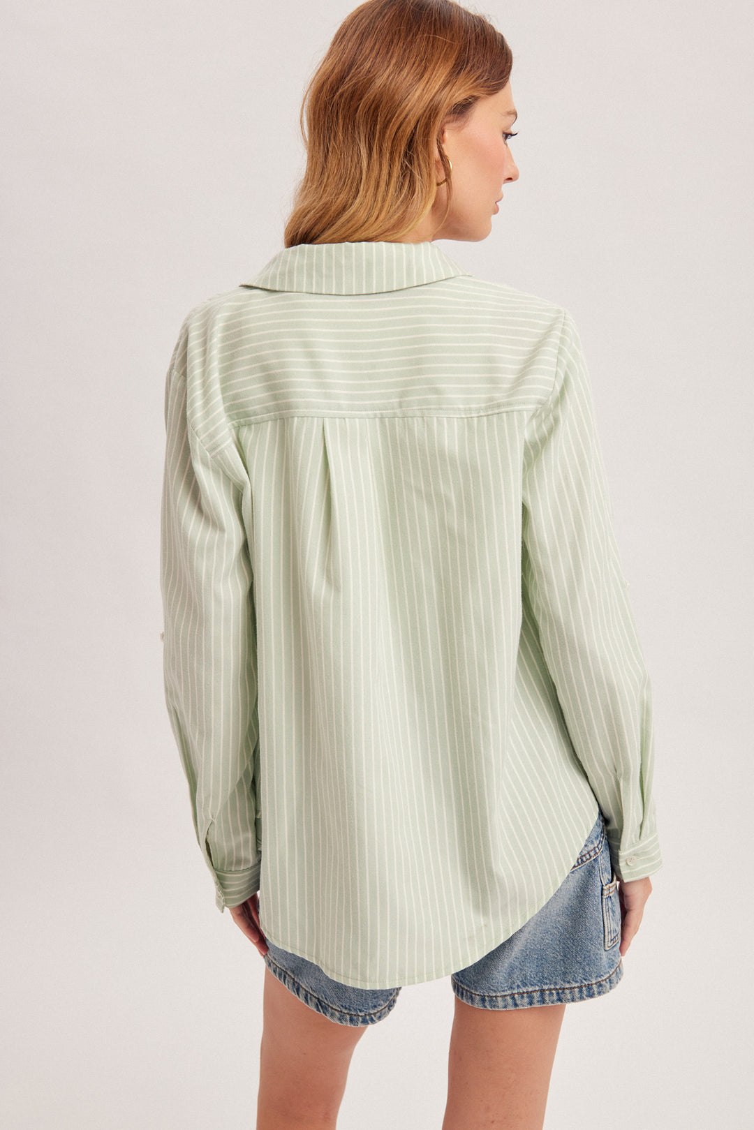 Woman wearing a light green striped shirt with denim shorts on a plain background