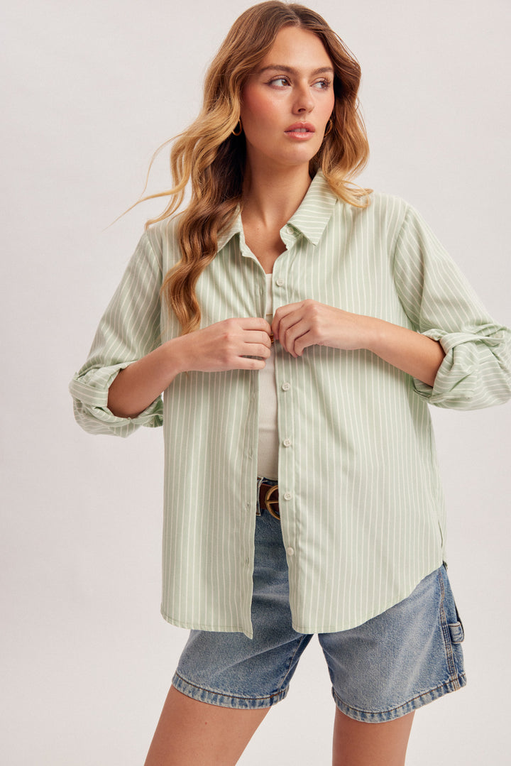 Woman wearing a light green striped shirt and denim shorts on a plain background