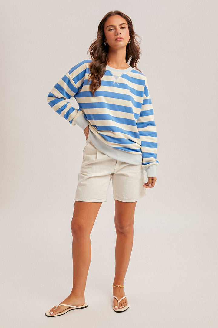 Woman wearing a blue and white striped sweater and white shorts on a plain background