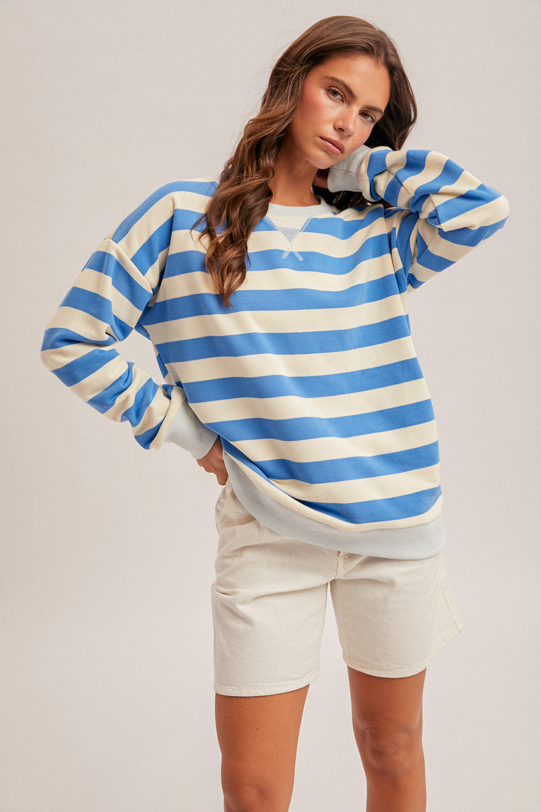 Woman wearing a blue and white striped sweater with beige shorts on a plain background