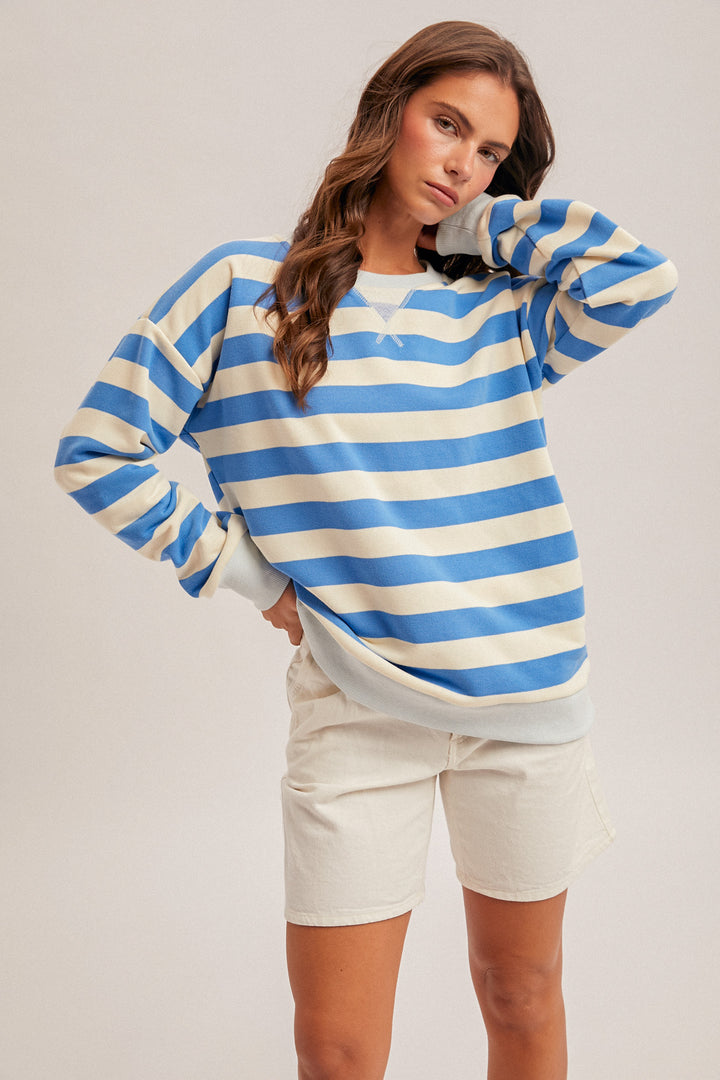 Woman wearing a blue and white striped sweater with beige shorts on a plain background