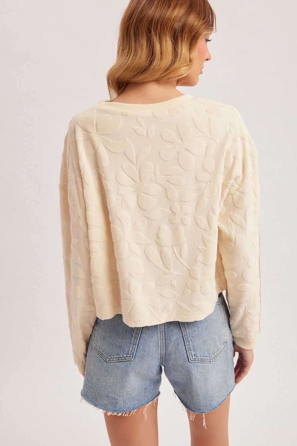 Woman wearing a cream cable knit sweater and denim shorts on a plain background