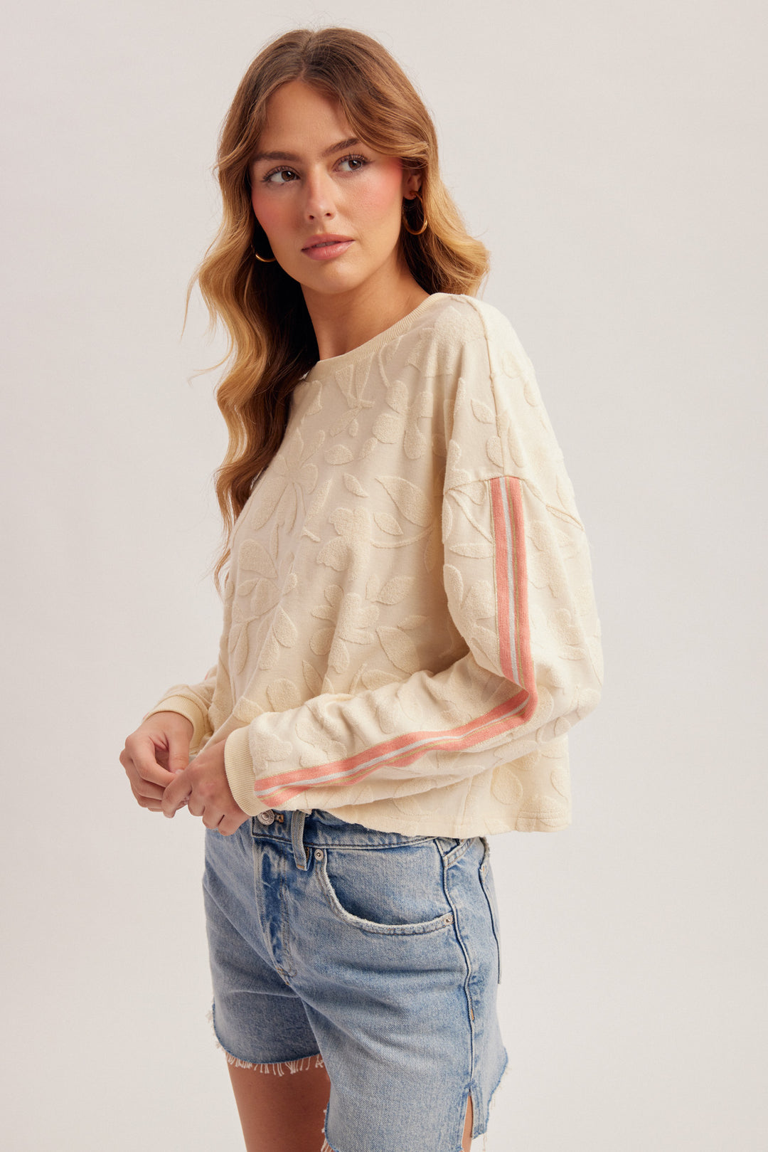 Woman wearing a beige sweater with pink stripes and denim shorts on a white background